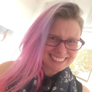 a selfie of the artist. thye have long pink hair and glasses and a big smile